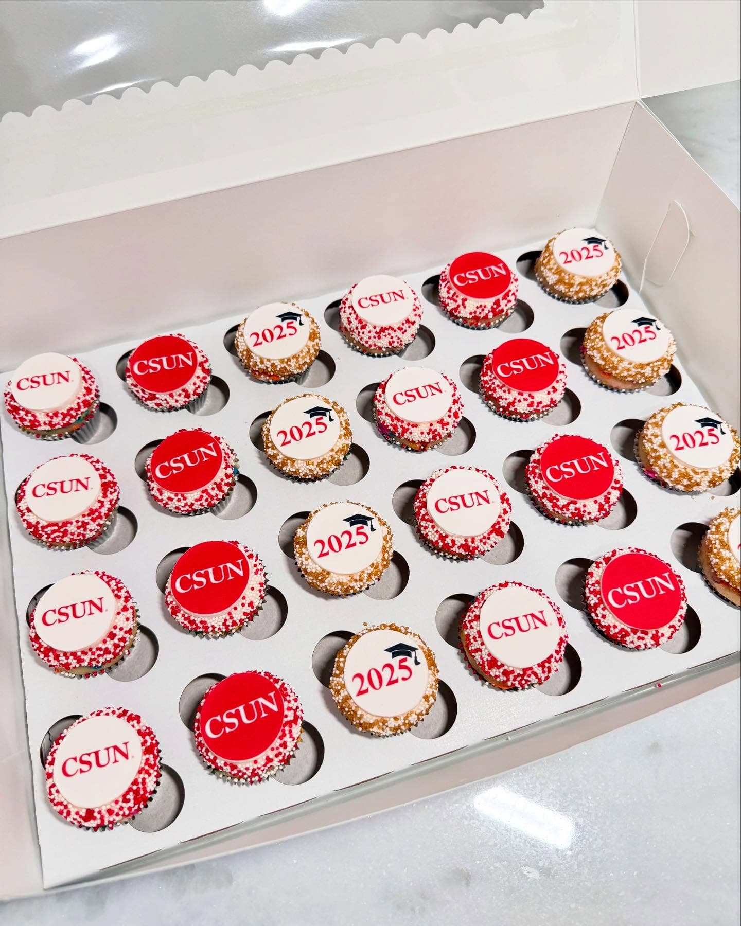 Box of red and white CSUN class of 2025 graduation cupcakes with edible logos